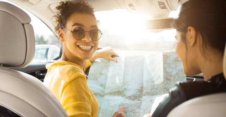 smiling woman holding up a map in the driver's seat of her car