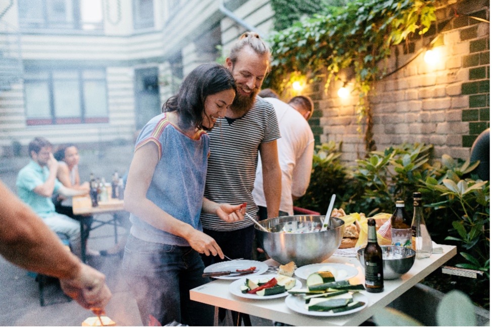 Man and woman in a backyard grabbing food from table